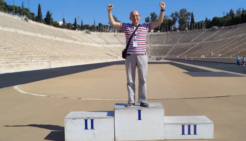 Mężczyzna z podniesionymi rękami na podium w historycznym stadionie panatenajskim.