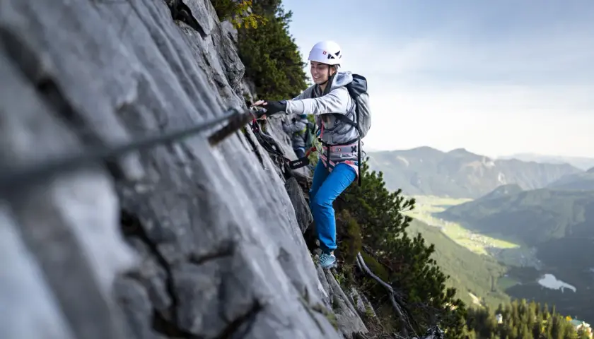 Uśmiechnięta kobieta na via ferrata dla początkujących, z widokiem na dolinę.