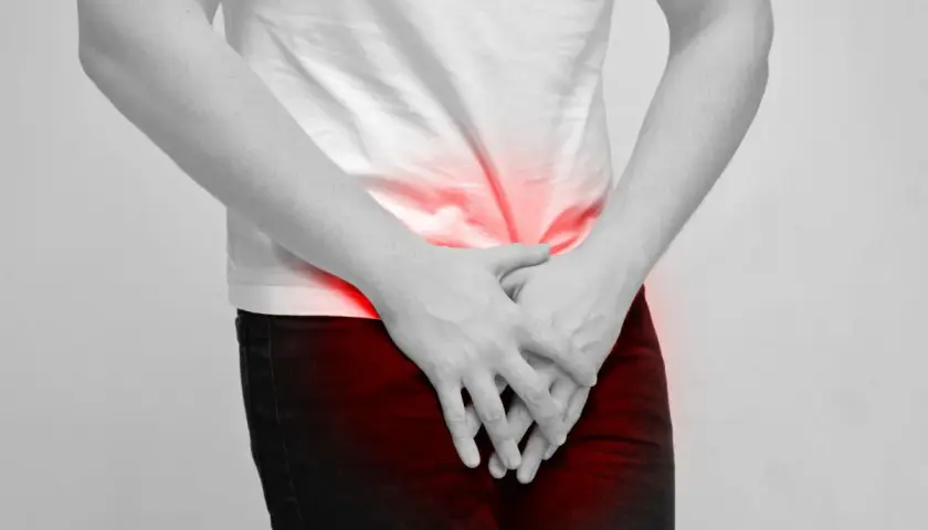 Mężczyzna trzyma ręce na podbrzuszu, gdzie widoczne są czerwone plamy bólu. Może to symbolizować dyskomfort związany z masowaniem prostaty.
