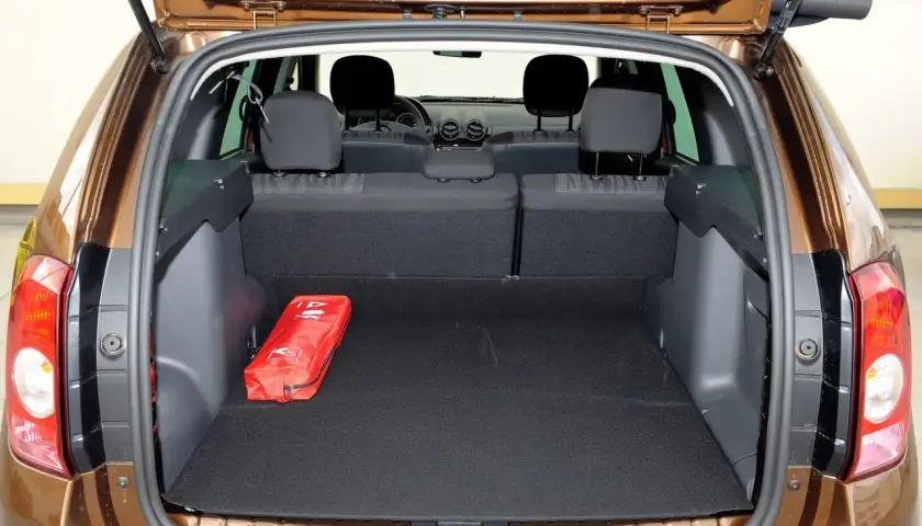 Otwarty bagażnik Dacia Duster, pokazujący jego pojemność. Czerwona apteczka leży na czarnym dywaniku.