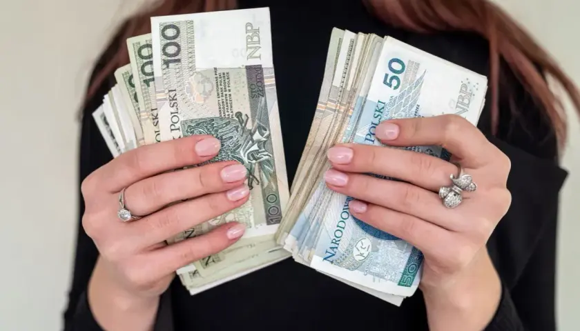 Pracownik socjalny trzyma w dłoniach pliki banknotów 100 i 50 złotowych.