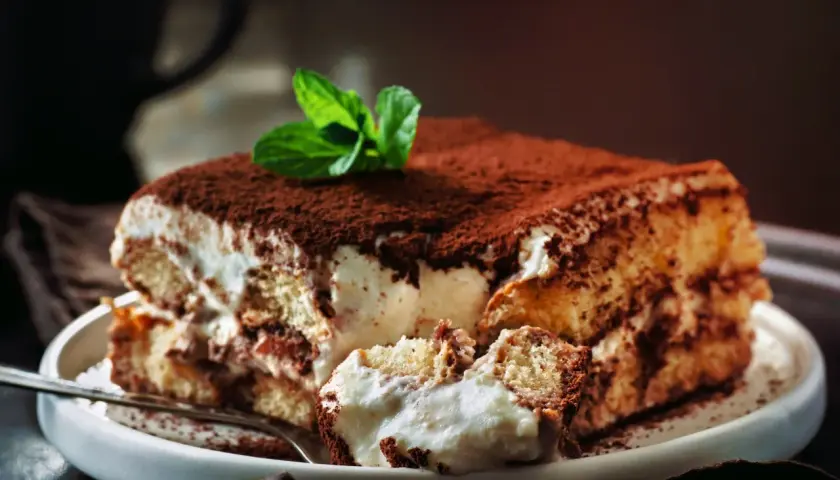 Pyszne tiramisu bez jajek, posypane kakao i udekorowane listkiem mięty, czeka na widelcu.