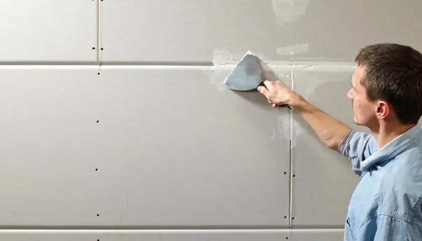 Mann spachtelt Rigipsplatten, um eine glatte Wand zu schaffen.