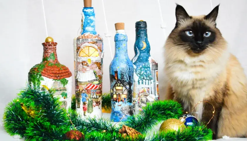 Urocze butelki ozdobione techniką decoupage na szkle, z zimowymi scenkami. Obok siedzi piękny kot.