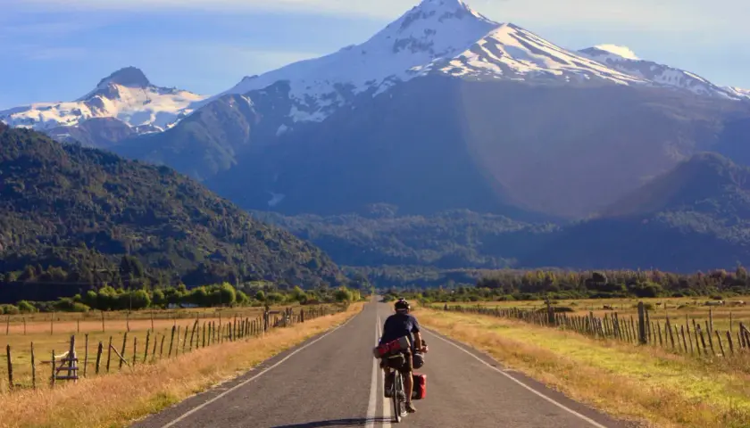 Ciclista pedaleando por la Carretera Austral, con imponentes montañas nevadas de fondo.