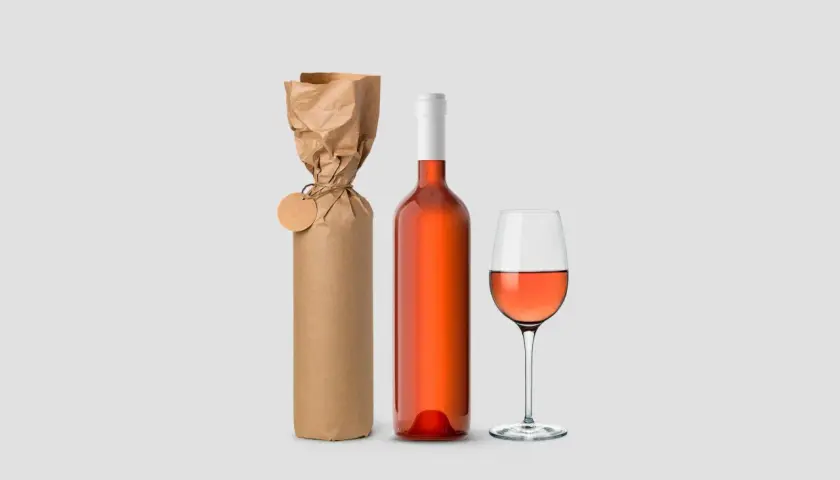 Eine Weinflasche verpacken: Eine Flasche Roséwein neben einer in braunes Papier eingewickelten Flasche mit Anhänger und einem Weinglas.