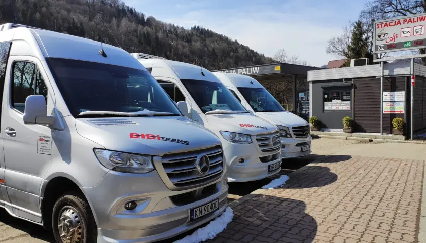 Trzy białe busy marki Mercedes stojące pod zadaszeniem stacji paliw.