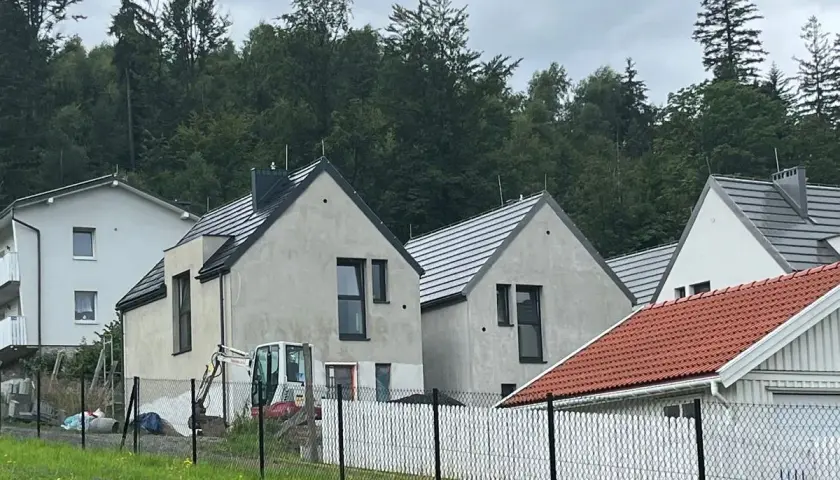 Nowe domy w stylu skandic hus, w budowie, z koparką na placu. W tle las.