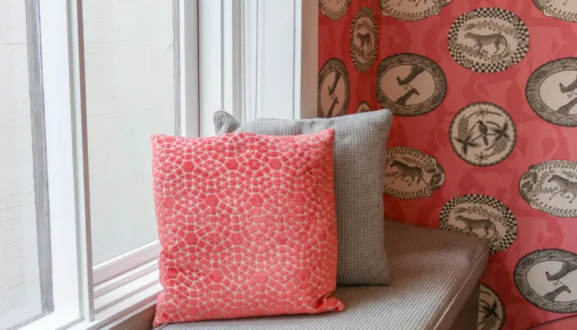 Färgglad tapetsera non woven med djurmotiv i ovala ramar. Två kuddar, en korallfärgad och en grå, vilar på en fönsterbänk.