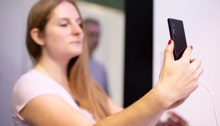 Kobieta z długimi blond włosami trzyma smartfon, na którym widać **aplikację Tuya po polsku**.