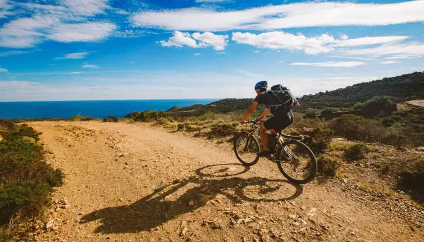 Ciclista disfruta de rutas en bici con encanto por la costa mediterránea. El mar azul y el cielo despejado acompañan su aventura.