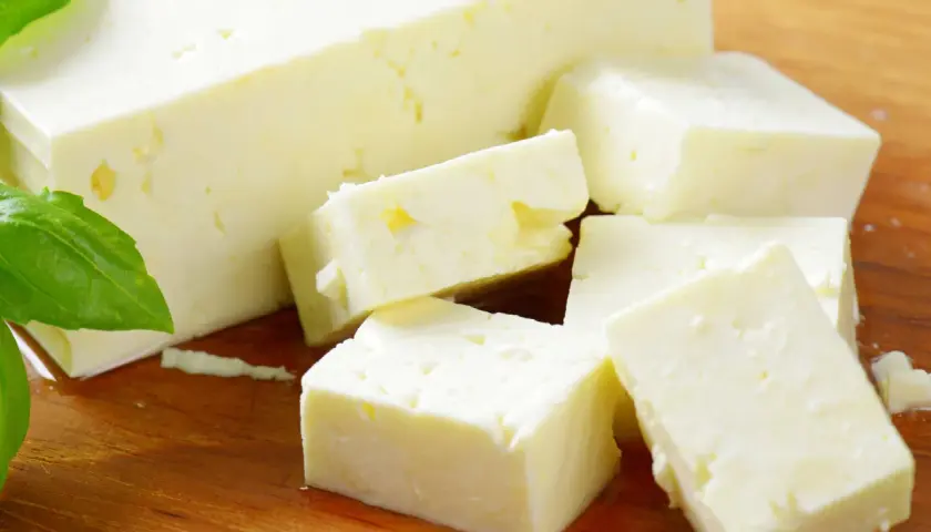 Frischer Feta, leicht schleimig, liegt auf einem Holzbrett, daneben grüne Basilikumblätter.