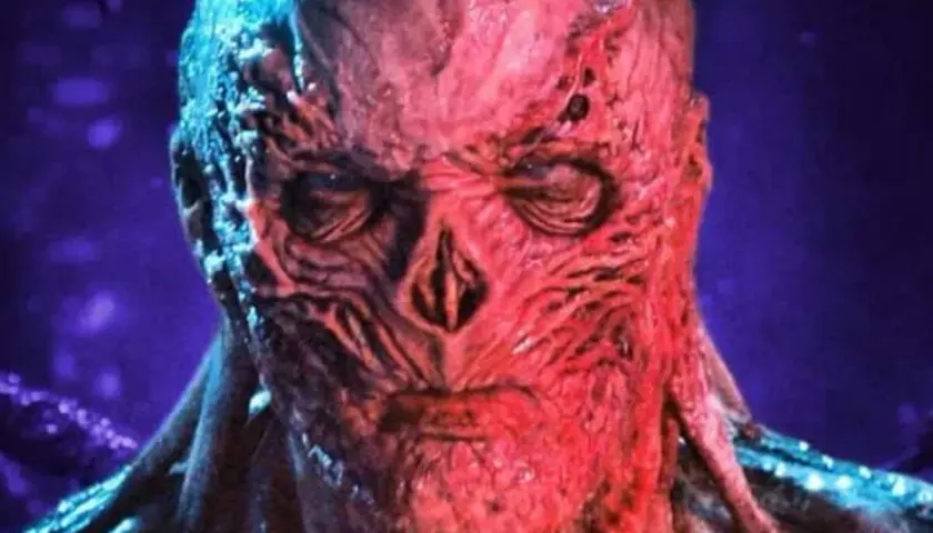 Le visage déformé et rougeaud de Vecna, le monstre de Stranger Things, se détache sur un fond violet.