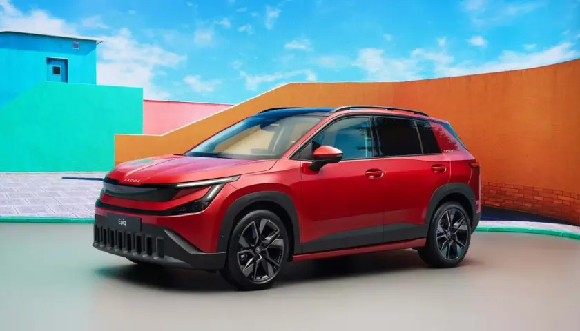 La Skoda Epiq rossa, un SUV compatto, si presenta con un design audace e moderno, circondata da un'architettura colorata e un cielo azzurro.