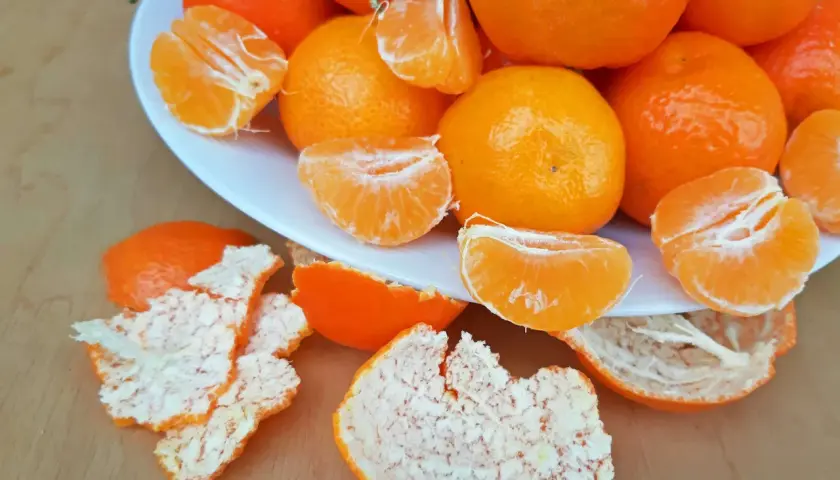 Ein Teller voller saftiger Mandarinen, einige geschält und in Spalten geteilt, daneben die orangen Schalen. Perfekt zum Lagern und Genießen.