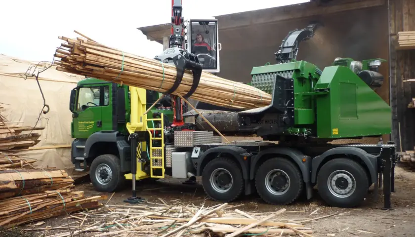 Grüner Holzhacker LKW mit Kran lädt Holzstämme. Der Hacker zerkleinert Holz zu Hackschnitzeln.