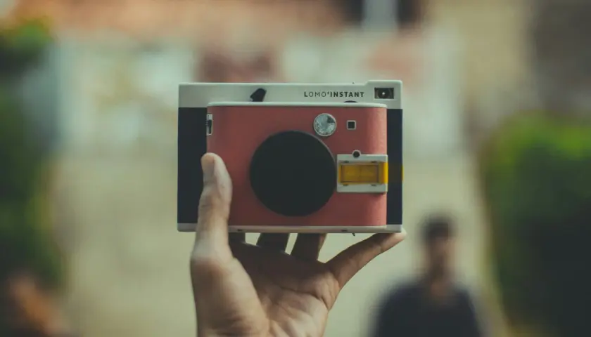 Una mano tiene una Lomo'Instant. Cosa significa "fotocamera ai"? Questa fotocamera istantanea, con il suo design retrò, cattura momenti unici.