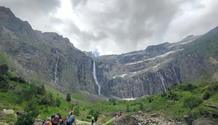 Senderos de Gavarnie: excursionistas caminan hacia impresionantes cascadas en un valle montañoso.