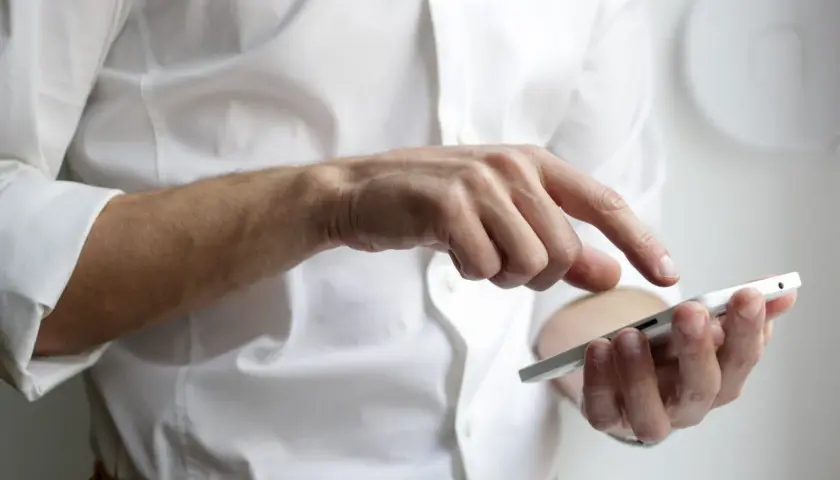 Mężczyzna w białej koszuli prowadzi rozmowę telefoniczną po angielsku, dotykając ekranu smartfona.
