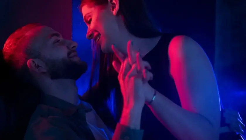 Para zbliża się do siebie w blasku neonów. Ich dłonie splatają się, tworząc intymną chwilę, która sugeruje seks bez penetracji.
