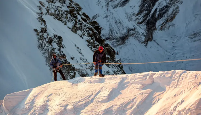 Dwóch alpinistów na śnieżnym grzbiecie, przygotowuje się do wspinaczki na Mera Peak. Słońce oświetla zbocza.