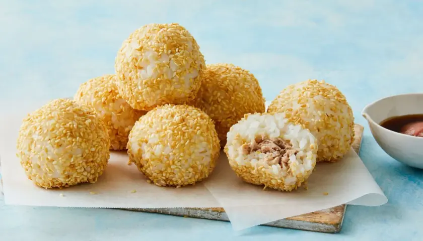 A delicious tuna bento box features rice balls coated in sesame seeds, with one cut open to reveal the tuna filling.