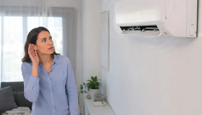 Mujer escucha atentamente el **ruido del aire acondicionado**, preocupada por un sonido inusual.