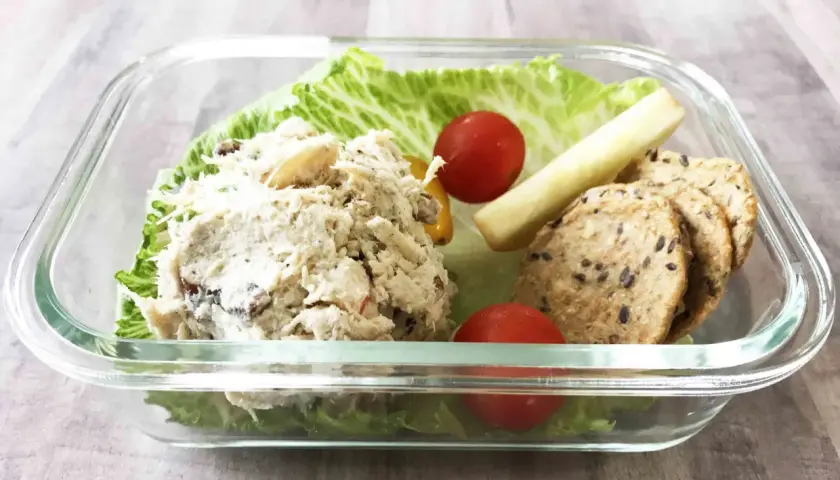A delicious chicken salad bento box with lettuce, cherry tomatoes, a pickle spear, and crackers.
