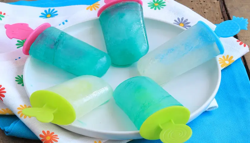 Cinque ghiaccioli senza zucchero, colorati e rinfrescanti, su un piatto bianco, pronti per un'estate sana e gustosa.