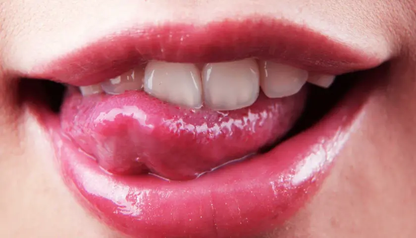 Labbra lucide e lingua che esce, mostrando i denti. La saliva è disinfettante, un piccolo segreto di bellezza naturale.