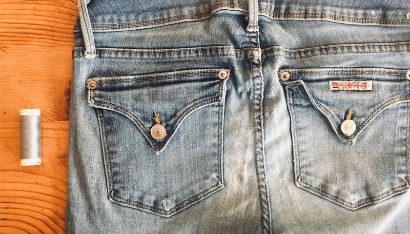 A spool of grey thread sits beside the back pockets of light blue jeans, ready for invisible mending.