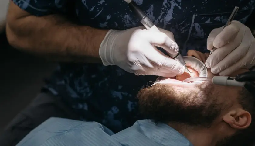 Dentysta w białych rękawiczkach używa wiertła i narzędzi, by oczyścić zęby pacjenta. To właśnie robi fleczer, co to za zabieg?