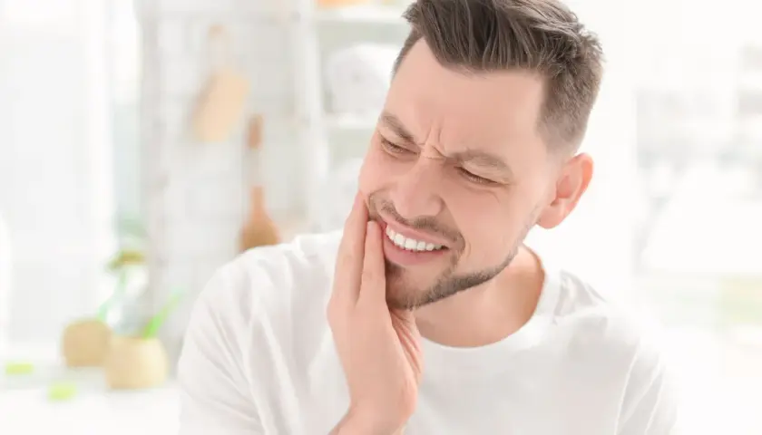 Uomo con mano sulla guancia, espressione di dolore ai denti, forse un problema al solco gengivale.