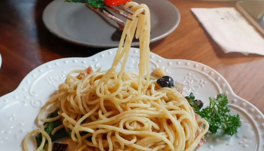 Widok z bliska na talerz pysznego spaghetti aglio e olio, z widelcem unoszącym porcję makaronu z bazylią i pomidorkiem.