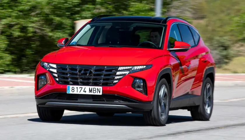 Un conductor prueba el Hyundai Tucson híbrido enchufable rojo, con su distintiva parrilla y luces LED, circulando por una carretera.