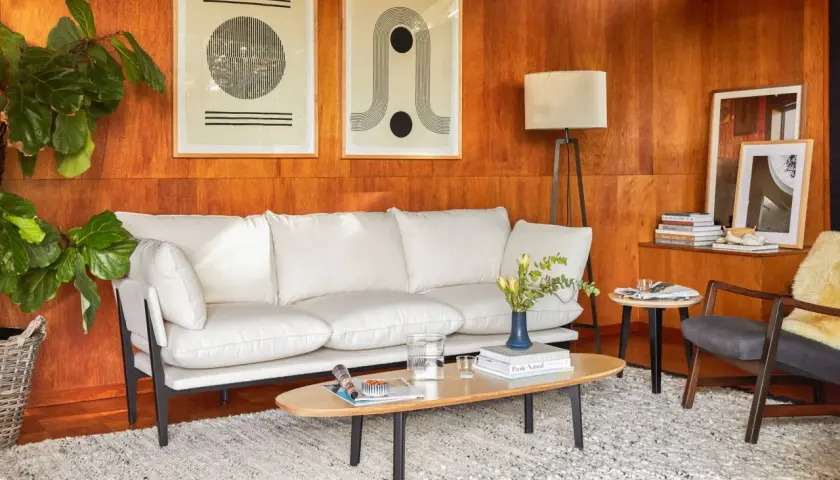 A modern living room with a white sofa, art, and a floor lamp, all set against warm wood tones.