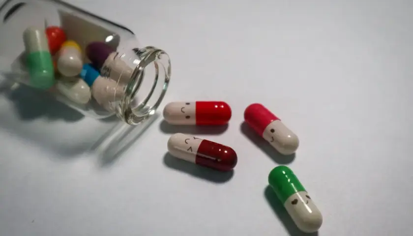 Kapsułki z uśmiechniętymi buźkami obok szklanej buteleczki z lekami.