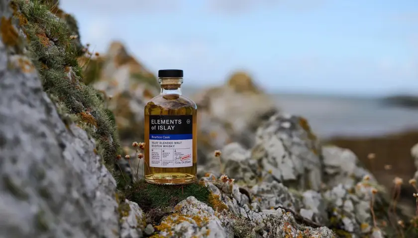 Bouteille de whisky "Elements of Islay" posée sur des rochers moussus, évoquant l'atmosphère sauvage de la distillerie Islay.
