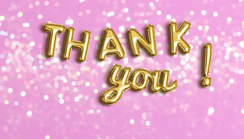 Globos dorados forman las palabras de agradecimiento "Thank you!" sobre un fondo rosa con luces bokeh.