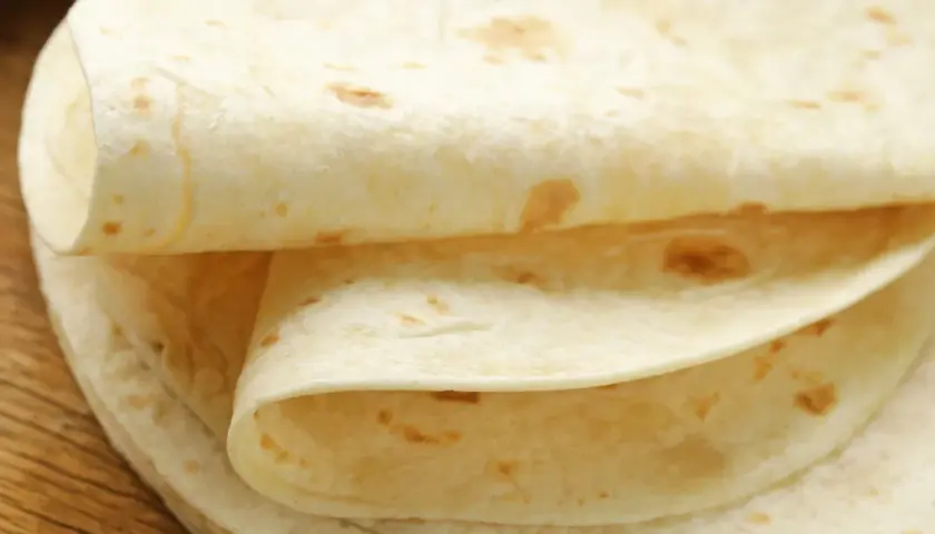 Stos cienkich, jasnych placków tortilli na drewnianym blacie. Czy tortilla jest zdrowsza od chleba? Zależy od składników!