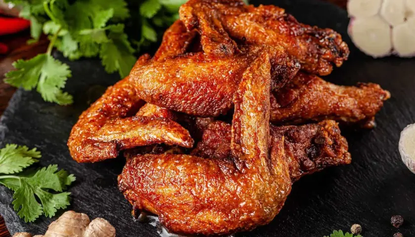 Alette di pollo al forno dorate e succulente, servite su una pietra scura con coriandolo fresco, zenzero e aglio.