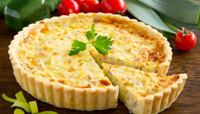 Quiche Lorraine con pasta sfoglia, un classico della cucina francese, con una fetta tagliata per mostrare il ripieno cremoso e saporito.