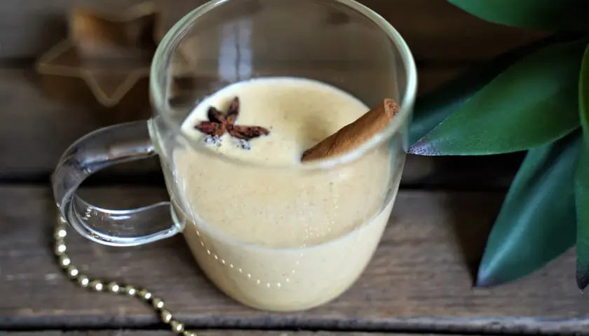 Un verre de lait de poule crémeux, garni d'anis étoilé et d'un bâton de cannelle, sur fond de bois rustique.