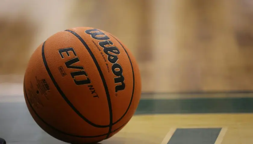 Pomarańczowa piłka Wilson Evo NXT leży na parkiecie hali sportowej, gotowa do gry.