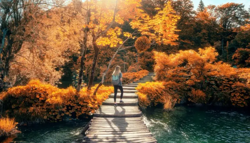 Frau wandert auf Holzsteg durch Herbstlaub in Kroatien. Das Wetter im Oktober ist sonnig und warm, perfekt für diese malerische Landschaft.