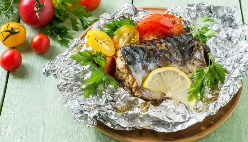 Poisson barbecue en papillote, servi avec des tomates et du persil, garni d'une tranche de citron.