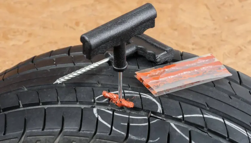 Kit de réparation pour pneu de voiture : un outil insère une mèche dans un pneu crevé.
