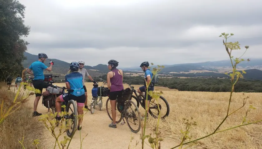 Ciclistas en ruta por la EuroVelo 6, disfrutando del paisaje rural y las colinas bajo un cielo nublado.
