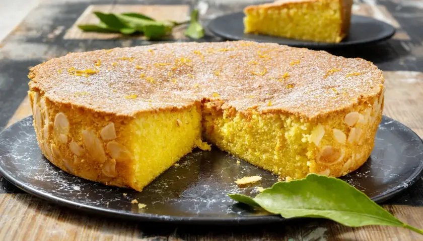 Deliziosa caprese al limone, con mandorle tostate sui bordi e scorza d'arancia in superficie, spolverata di zucchero a velo.