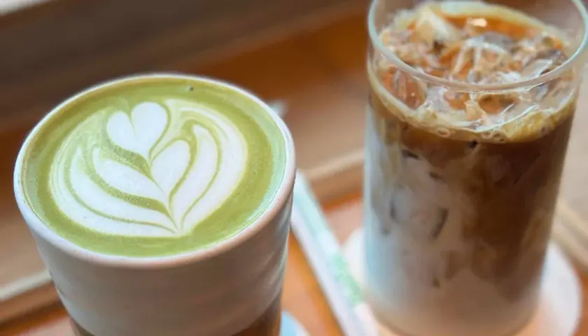 Grüner Matcha Latte mit Herz-Muster neben einem Eiskaffee. Der Matcha Mate Unterschied wird hier visuell dargestellt.